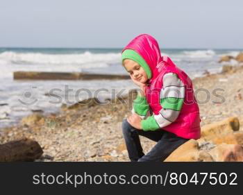 Girl sitting on the rocky beach and the sea happily lost in thought looking down