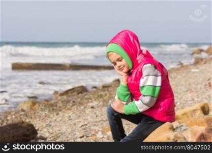 Girl sitting on the rocky beach and the sea happily lost in thought looking down