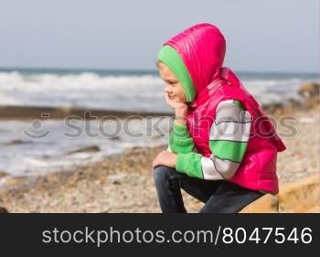 Girl sitting on the rocky beach and the sea head on his hand looking to the frame