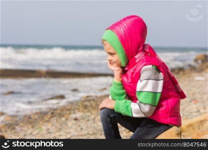 Girl sitting on the rocky beach and the sea head on his hand looking to the frame