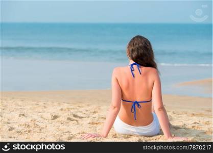 girl sitting on the sandy beach and looking at the ocean