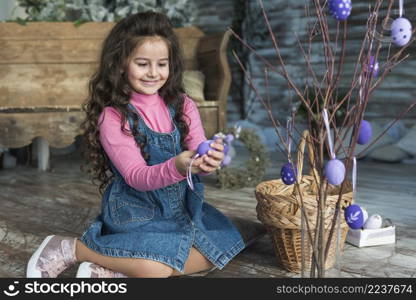 girl sitting with easter egg near branches vase