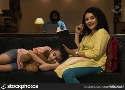 Girl sleeping on sofa while her mother looking at camera with holding a book and father using laptop