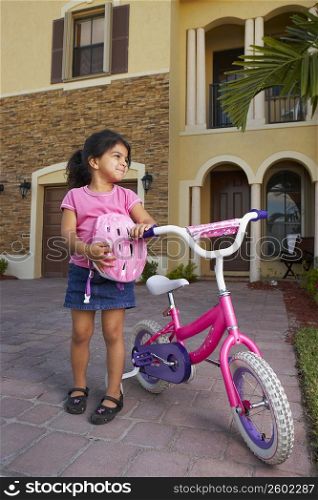 Girl standing and holding a bicycle in front of a house