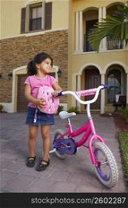 Girl standing and holding a bicycle in front of a house