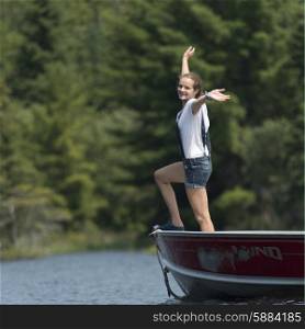 Girl standing on boat with her arms outstretched, Lake of the Woods, Ontario, Canada