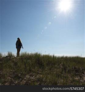 Girl standing on grassy sand dune under bright sunshine at Cavendish Dunelands Trail, Green Gables, Prince Edward Island, Canada