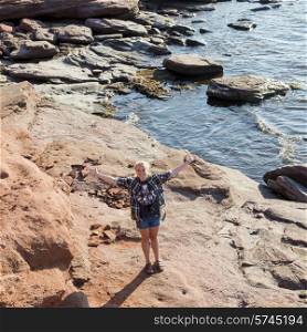 Girl standing with arm outstretched on rocky coastline, Green Gables, Cavendish, Prince Edward Island, Canada