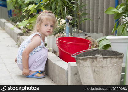 Girl stands in the yard of about watering the crane. The girl holding the bucket in his hands, and looks in the frame