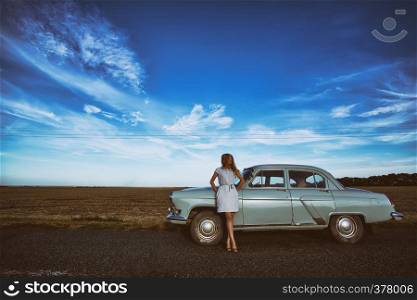 girl stands near a retro car, the background field, and a bright blue sky
