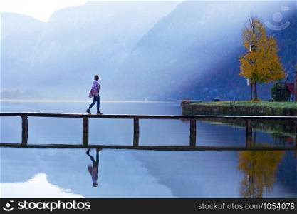 girl stands on a wooden bridge on a mountain lake in the early morning. beautiful landscape and reflection