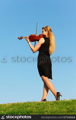 girl stands on grass and plays violin against sky