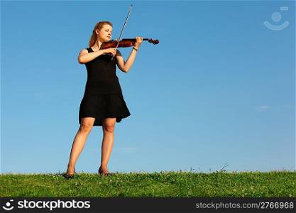 girl stands on grass and plays violin against sky