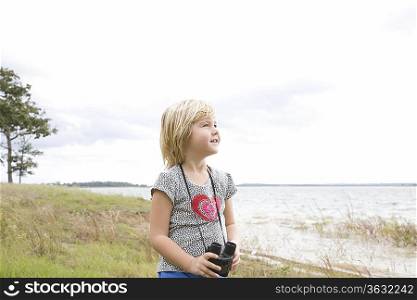 Girl stands with binoculars at lakeside