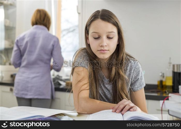 Girl studying at table with mother standing in background