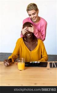 Girl surprising her female best friend. Model covering her eyes and hugging from behind. Two surprised girls. Women having fun and showing face emotions