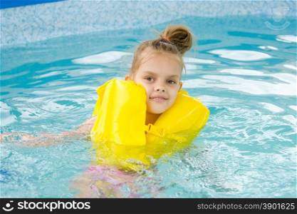 Girl swimming in the pool in the lifejacket. Six year old girl Europeans bathed in a small suburban pool