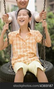 Girl swinging on a tire swing with her father standing behind her