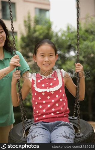 Girl swinging on a tire swing with her mother standing behind her