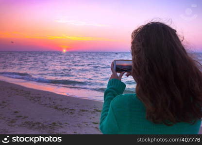 Girl takes pictures on the smartphone sunrise at the sea