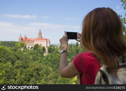 girl taking a picture of a beautiful castle on a hill with her smartphone