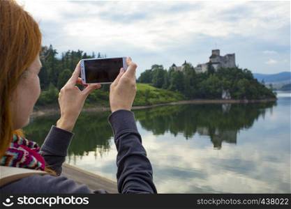 girl taking a picture of a beautiful castle on a lake shore with her smartphone