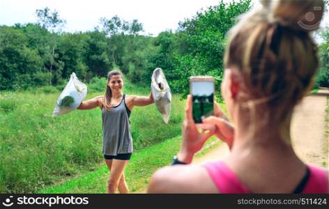 Girl taking a picture of a friend with trash bags after plogging. Selective focus on girl in background. Girl taking picture of a friend after plogging