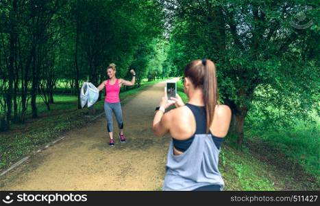 Girl taking a picture of a friend with trash bags after plogging. Selective focus on girl in background. Girl taking picture of a friend after plogging