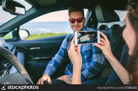 Girl taking a picture with the cell phone to her boyfriend in the car. Selective focus on mobile in foreground. Girl taking picture with mobile to her boyfriend