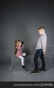 girl taking boy with camera against gray background