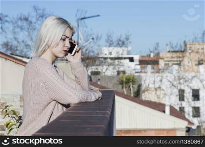 Girl talking on a smartphone while standing on the balcony.