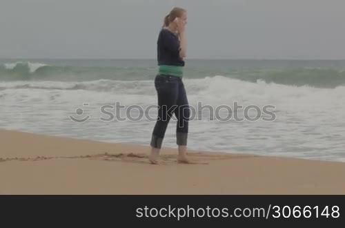 Girl talking on phone at the beach, wide shot.