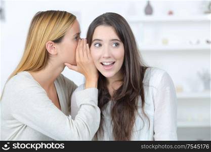 girl telling a secret in the ear of her friend