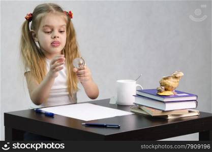 girl thoughtfully and effortlessly turns a small glass globe, sitting at the table. There are tombs of books, sheets of paper, a pen, glass globe, with a glass of tea, sea shell. The image of the writer.