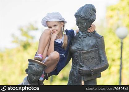 Girl thoughtfully sitting on the monument to the first teacher. Girl climbs first teacher sculpture located in the Krasnoarmeysk district of Volgograd Boulevard Engels