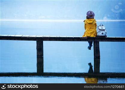 girl tourist in a hat and with a backpack sitting on a wooden bridge on a mountain lake in the early morning. beautiful landscape and reflection. Hallstatt