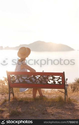 girl tourist sitting on a bench at the observation deck and looks at the sea and a beautiful landscape On the Sunset, Corfu Island in Greece