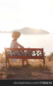 girl tourist sitting on a bench at the observation deck and looks at the sea and a beautiful landscape On the Sunset, Corfu Island in Greece