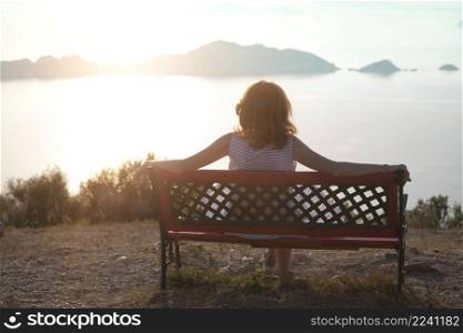 girl tourist sitting on a bench at  the observation deck and looks at the sea and a beautiful landscape On the Sunset, Corfu Island in Greece 