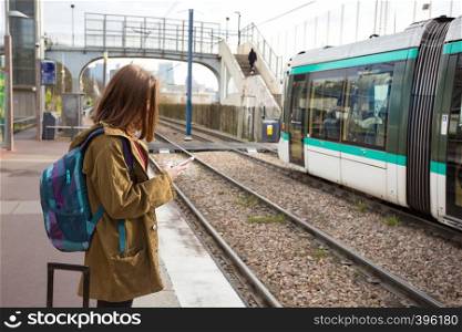 girl tourist with a backpack and a big yellow suitcase stands on the platform and waits for the train