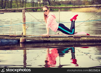 Girl training in sporty clothes on lake shore. Sports and activities concept. Slim fit attractive woman exercising stretching outdoor. Young motivated girl training in sporty clothes on lake shore