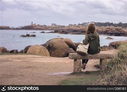 girl traveler sits on a bench near the sea and the shore at the Tregastel, Brittany. France
