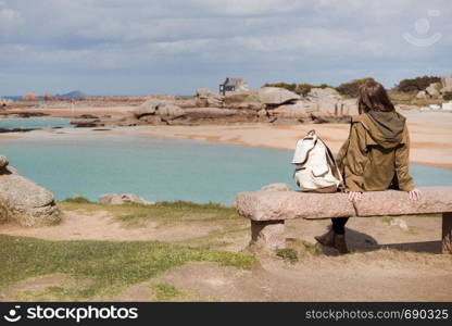 girl traveler sits on a bench near the sea and the shore at the Tregastel, Brittany. France