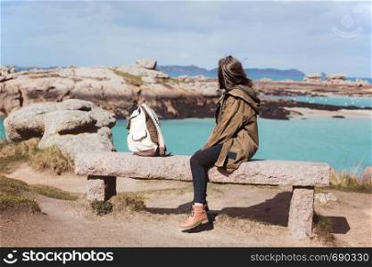 girl traveler sits on a bench near the sea and the shore at the Tregastel, Brittany. France