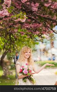 Girl under the sakura tree with flowers in hands enjoys the blossom. Smiling girl under sakura blossoms