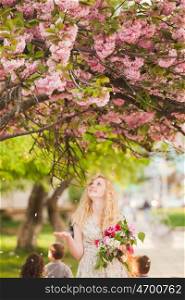 Girl under the sakura tree with flowers in hands enjoys the blossom. Smiling girl under sakura blossoms