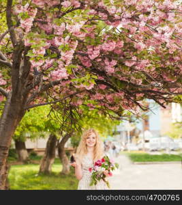 Girl under the sakura tree with flowers in hands enjoys the blossom. Smiling girl under sakura blossoms