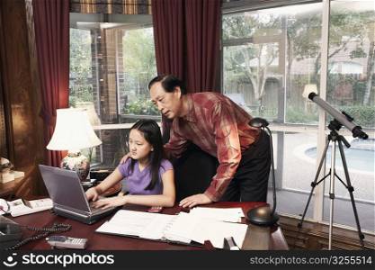 Girl using a laptop with her grandfather standing beside her