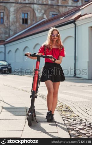 Girl using electric scooter in the street in downtown rented by using service on smartphone. Candid people, real moments, authentic situations
