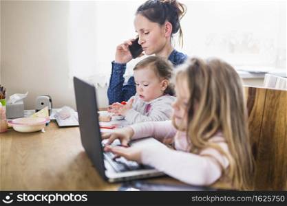 girl using laptop beside her mother talking smartphone